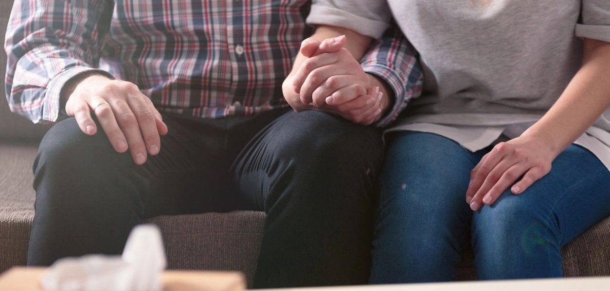 a man and a woman sitting on a couch holding hands.