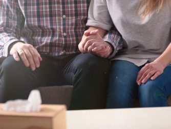 a man and a woman sitting on a couch holding hands.