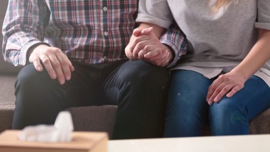 a man and a woman sitting on a couch holding hands.